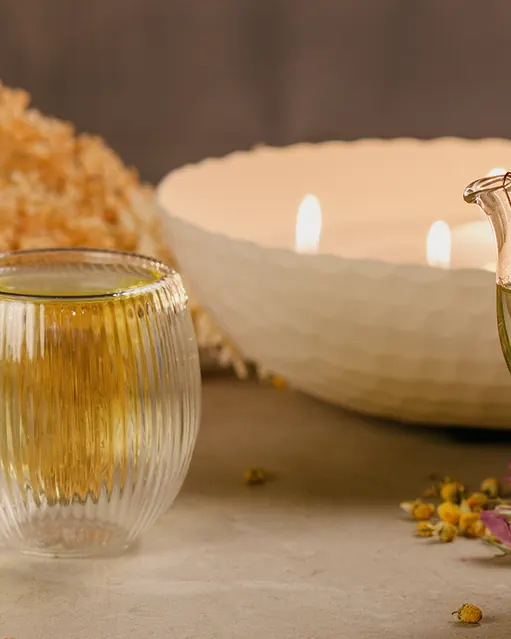 قوری دمنوش کنار شمع روشن و گل‌های خشک در نور آرام شب