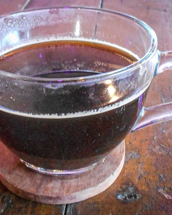 آمریکانوی آماده در لیوان شیشه‌ای روی میز چوبی کافه