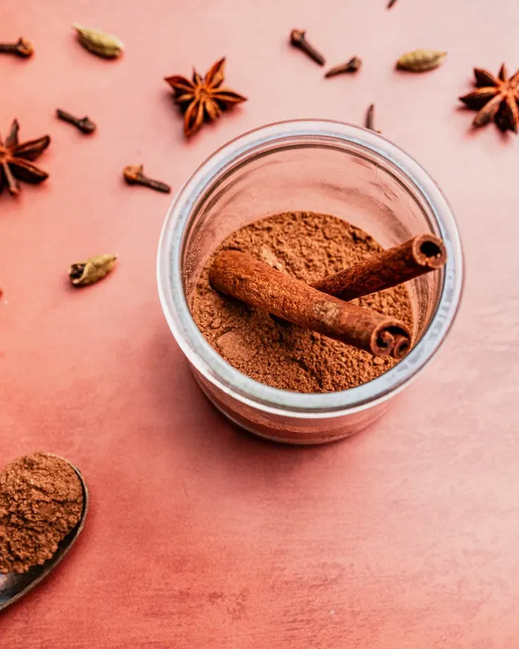 شیشه پودر دارچین با چوب دارچین کنار میخک، هل و انیسون ستارهای