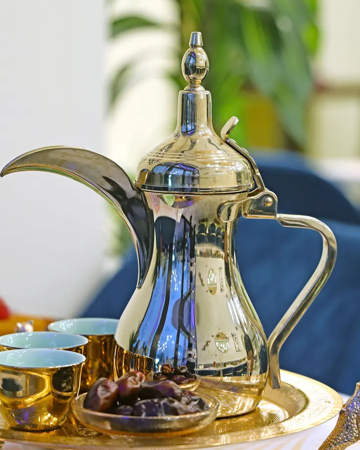 پارچ سنتی طلایی با فنجانهای کوچک و کاسه خرما روی سینی فلزی