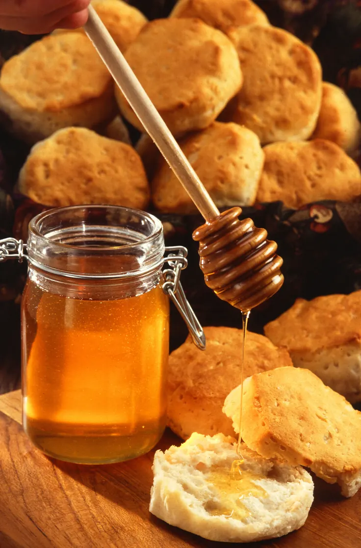 شیشه عسل طبیعی و قاشق عسلکش چوبی کنار شیرینی خانگی