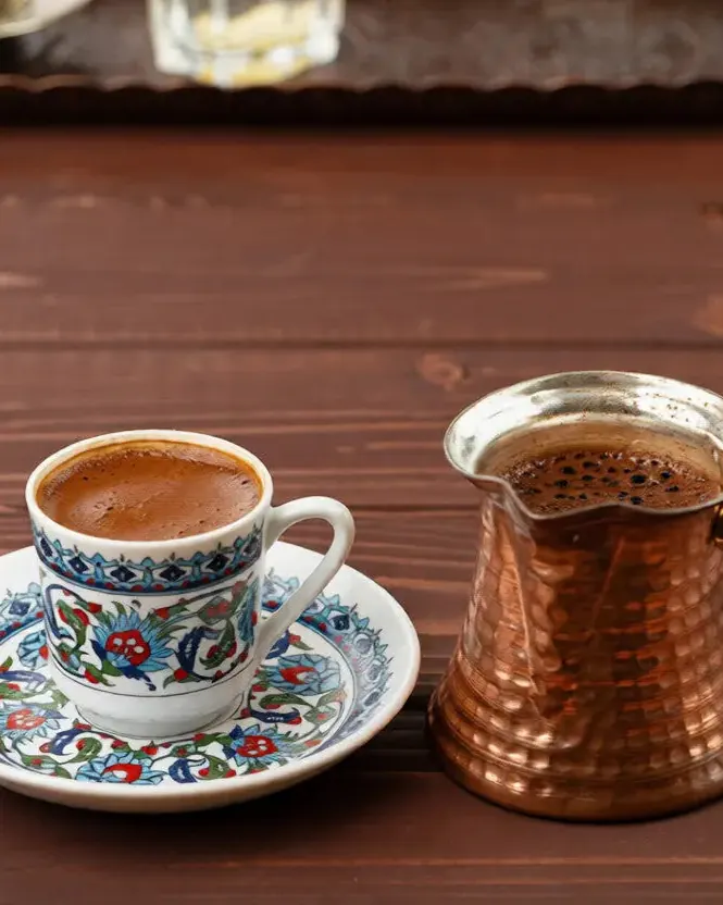 فنجان قهوه با نقشهای سنتی کنار جذوه مسی چکشخورده روی میز چوبی