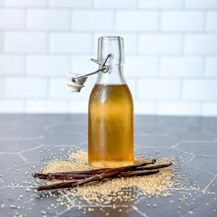 شیشه شربت وانیل خانگی کنار تکه وانیل و شکر