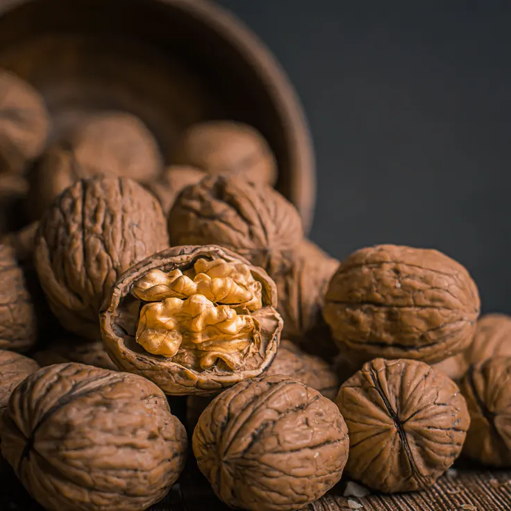 مغز گردوی تازه و نصفه داخل پوسته‌اش روی میز چوبی، ماده اولیه قهوه گردو